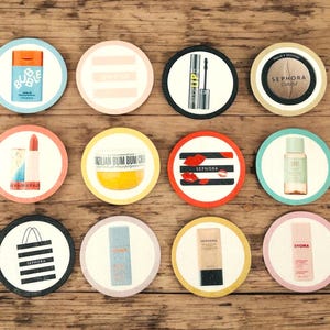 May include: A selection of circular coasters showcasing beauty products. The coasters feature images of makeup, skincare, and branded items, such as lipstick, mascara, and a shopping bag. The coasters are displayed on a wooden surface.