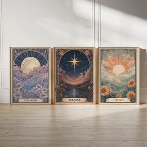May include: Three framed art prints featuring celestial themes. The prints depict the moon, a star, and the sun, each with floral and cloud details. The text on the prints reads "THE MOON", "THE STAR", and "THE SUN". The frames have a vintage aesthetic.