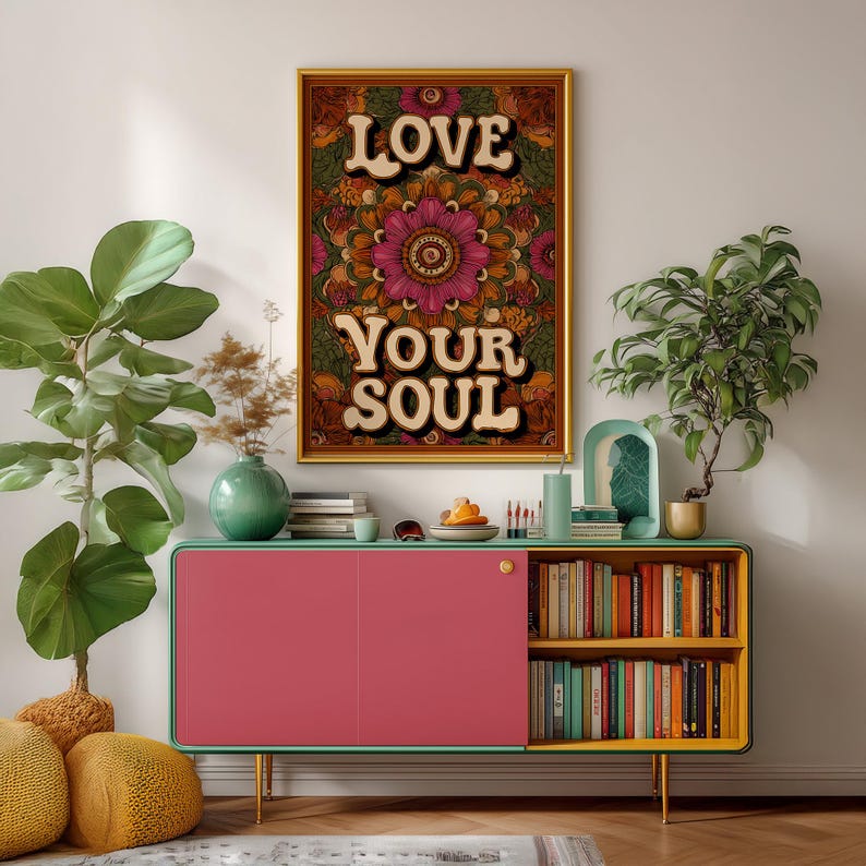 Puede incluir: Un cuadro enmarcado con las palabras "LOVE YOUR SOUL" en una fuente retro. La obra de arte presenta un dise&ntilde;o floral de mandala en tonos de rosa, naranja y verde. La impresi&oacute;n se muestra encima de un mueble rosa y amarillo con libros y plantas.
