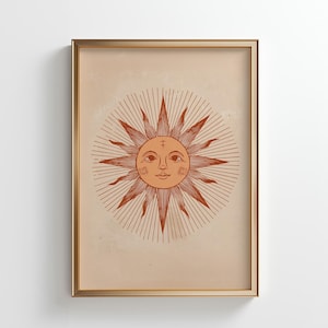 May include: Framed art print featuring a stylized sun illustration in shades of orange and brown. The sun has a smiling face and radiating lines, set against a beige background. The artwork is enclosed in a gold-colored frame.