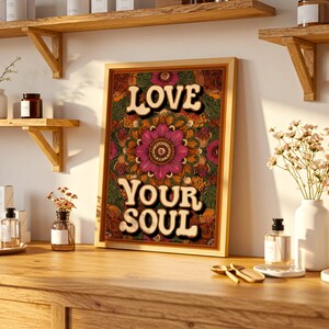 Puede incluir: Un cuadro enmarcado con las palabras "LOVE YOUR SOUL" en una fuente retro. La obra de arte presenta un dise&ntilde;o floral de mandala en tonos de rosa, naranja y verde, sobre un fondo oscuro. El marco es de color madera clara.