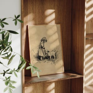 May include: A framed vintage print showing a child and a lamb. The black and white illustration depicts a young person in a dress standing next to a lamb in a grassy field. The artwork is set against a tan background and framed in light brown wood.