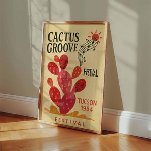 K&ouml;nnte beinhalten: Ein gerahmtes Poster mit hellgelbem Hintergrund zeigt den Text "CACTUS GROOVE FESTIVAL TUCSON 1984". Ein roter Kaktus mit Noten und eine Sonnengrafik sind ebenfalls abgebildet. Das Poster lehnt an einer Wand auf einem Holzboden.
