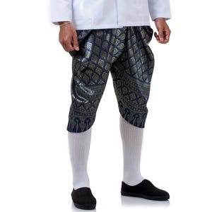 May include: A person is wearing a white shirt, blue and gold patterned capri trousers, white socks, and black shoes. The capri trousers have a detailed, ornate design. The outfit is set against a white background.