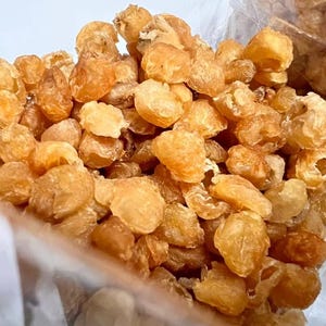 May include: A close-up of a bag of dried longan fruit. The fruit is light brown and has a wrinkled texture. The fruit is in a clear plastic bag.