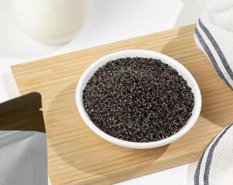 Może przedstawiać: Biała miska wypełniona ciemnym, ziarnistym proszkiem stoi na drewnianej desce do krojenia. Biały ceramiczny pojemnik w tle. Z prawej strony złożony biało-niebieski ręcznik w paski.