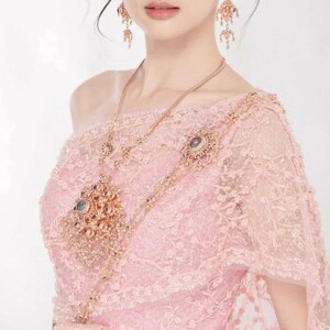 May include: A pink lace dress with a matching necklace and earrings set. The necklace features a large pendant with multiple gemstones. The earrings are dangling and ornate. The dress has a one-shoulder design.