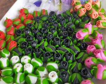 May include: A white platter displays an assortment of colorful, miniature rose buds and flowers. The roses are in shades of red, black, pink, and white, with green leaves. Purple and white flowers are also present.