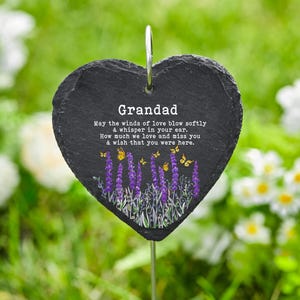 Puede incluir: Un marcador de jardín de pizarra negra en forma de corazón con la palabra "Grandad" y un mensaje sincero. El marcador presenta ilustraciones de lavanda morada y mariposas amarillas. Una estaca de metal sostiene el marcador.