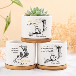 May include: White ceramic plant pots with a Winnie the Pooh illustration and the text "Never forget the difference you make." Each pot has a bamboo saucer. One pot has a succulent.