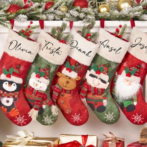 May include: Five Christmas stockings with white faux fur cuffs, each personalised with names Olivia, Trista, Dinah, Angel, and Joseph. The stockings feature red and green fabric with snowflake patterns and plush appliques of a penguin, snowman, reindeer, elf, and Santa.