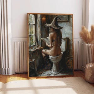 May include: A framed art print showing a person wearing a witch hat, seated on a toilet, reading a newspaper. The artwork has a vintage aesthetic with a muted colour palette, featuring a window and a lit candle.