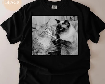May include: Black t-shirt with a black and white image of two cats. One cat holds a lighter, and the other has a cigarette in its mouth. The word "BLACK" is in a light tan circle in the upper left corner.