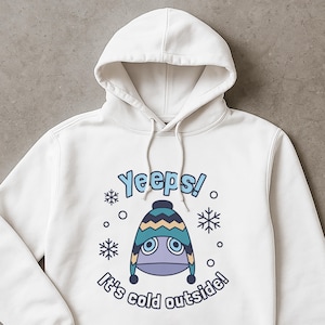 May include: White hooded sweatshirt with a graphic of a cartoon character wearing a winter hat. The text "Yeeps!" and "It's cold outside!" are printed in blue. Snowflakes and circles surround the character.