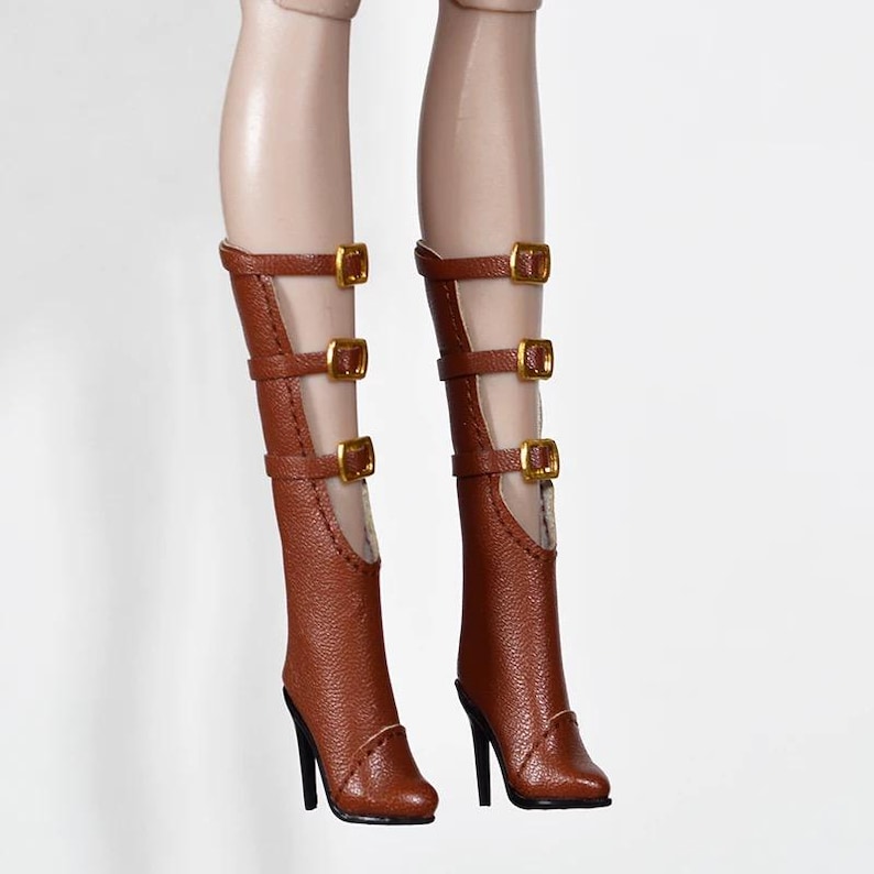 May include: Brown high-heeled boots with multiple straps and gold-colored buckles. The boots have a pointed toe and a stiletto heel. The boots are made of a textured material.