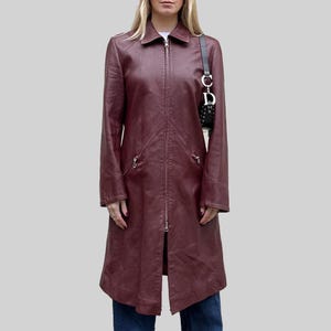 May include: A burgundy leather coat with a full-length zip. The coat features a collared neckline, long sleeves, and two zipped pockets. The knee-length coat has a slight A-line shape.