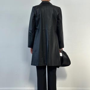 May include: A black leather coat with a tailored fit, paired with black trousers and a matching black handbag. The coat features a classic lapel and a knee-length design, suitable for various occasions.