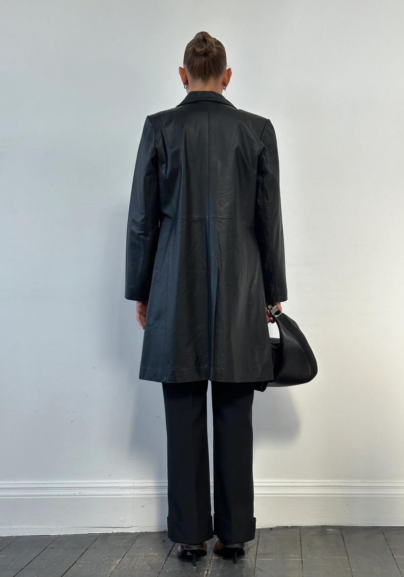 May include: A black leather coat with a tailored fit, paired with black trousers and a matching black handbag. The coat features a classic lapel and a knee-length design, suitable for various occasions.