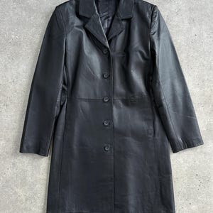May include: A black leather coat with a classic design. The coat features a notched collar, long sleeves, and a button-down front. The coat is approximately 40 inches long.