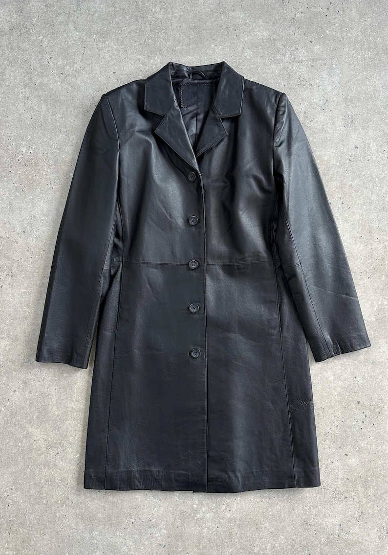 May include: A black leather coat with a classic design. The coat features a notched collar, long sleeves, and a button-down front. The coat is approximately 40 inches long.