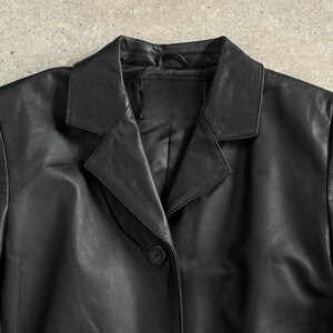 May include: A black leather blazer with a notched lapel collar and two button closure. The jacket has a classic design and is made of a smooth, shiny material. The blazer is a versatile piece of outerwear.