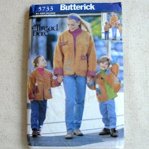 May include: A Butterick sewing pattern envelope, featuring a woman and two children wearing matching tan jackets with decorative patches and plaid cuffs. The envelope has the text "5733" and "Thread Bare".