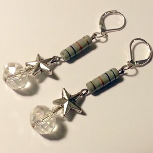 May include: A pair of dangle earrings featuring silver-toned leverback hooks, a cylindrical gray electronic resistor component with thin colored stripes, a five-pointed silver-toned star charm, and a clear faceted spherical glass bead at the base.