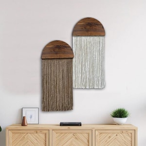 May include: Two wall hangings with wooden half-circle tops and long fringe. The fringe is brown and white.