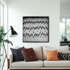 May include: A white couch with three throw pillows. The couch is in front of a white wall with a black and white abstract art print hanging above it.