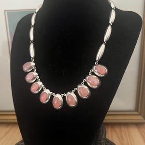 May include: A silver necklace with a chain of oval links and seven oval pink stones.