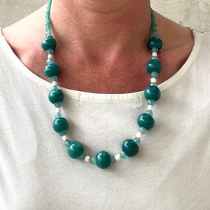 May include: A teal and white beaded necklace with large round beads. The necklace is made of glass beads and is approximately 18 inches long.