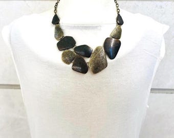 Peut inclure: Un collier imposant avec des pendentifs métalliques de forme irrégulière dans des tons bronze, or et gris foncé. Le collier est présenté sur un fond blanc, mettant en valeur son design et sa texture uniques. La chaîne est de couleur bronze foncé.