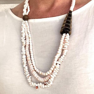 Puede incluir: Un collar de varias hebras hecho de cuentas de concha blanca con un colgante cónico marrón y negro.