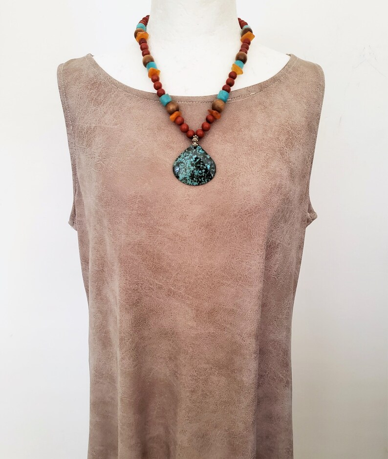 Puede incluir: Un collar de cuentas turquesa y marr&oacute;n con un gran colgante turquesa. El collar est&aacute; en un maniqu&iacute; de gamuza marr&oacute;n.