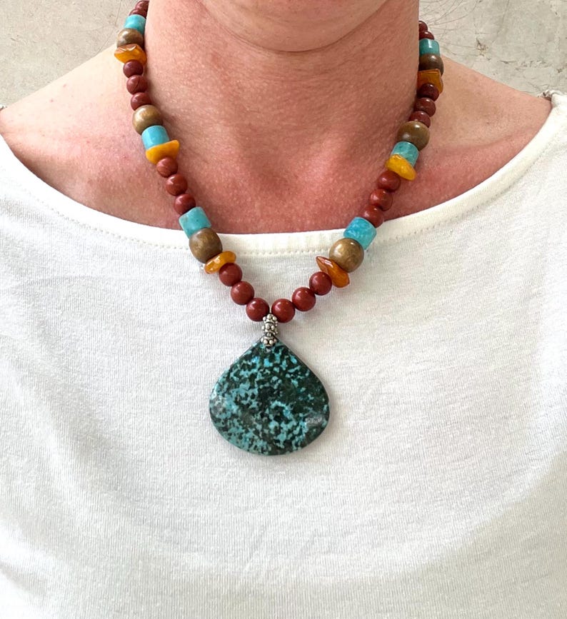 Puede incluir: Un collar de cuentas turquesa y marr&oacute;n con un gran colgante turquesa. El collar est&aacute; hecho con cuentas rojas, marrones y turquesas.