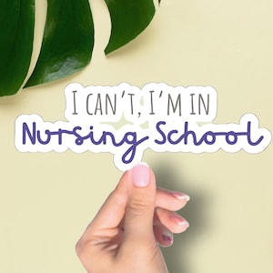 May include: A sticker with the text "I CAN'T, I'M IN Nursing School" in a handwritten style, held by a hand with manicured nails. The background is a light yellow with green leaves.