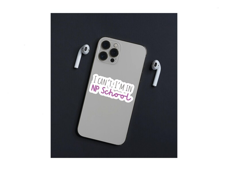 May include: A white iPhone with a sticker that says "I can't, I'm in NP School" in black and purple text. The phone is on a black surface with two white wireless earbuds.