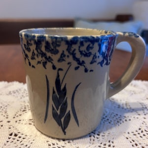 May include: A white ceramic mug with a black handle and the text "But First, Coffee" in a bold, black font. The mug is set against a neutral background, highlighting its simple design.