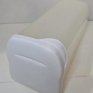 May include: A white rectangular bread box with a curved top and a white lid. The bread box is made of a smooth, solid material and is designed to store bread. The lid has a curved handle for easy opening.