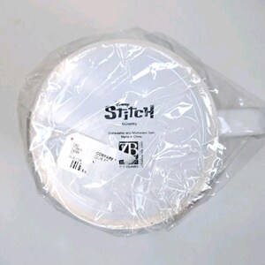 May include: A white ceramic mug with a handle, encased in clear plastic. The mug displays the word "Stitch" and the Disney logo. The mug is dishwasher and microwave safe.