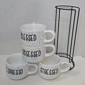 Puede incluir: Un juego de tres tazas de cerámica con un esmalte moteado de color crema. Cada taza presenta un diseño floral pintado a mano en tonos azules, verdes y amarillos. Las tazas tienen una forma simple y moderna con un asa cómoda.