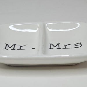 May include: A white ceramic dish with two compartments, featuring the words "Mr." and "Mrs." in black lettering. The dish has a rectangular shape with rounded edges, suitable for holding small items.