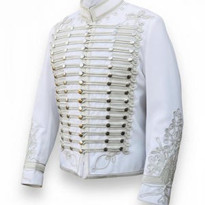 May include: A white military-style jacket with silver and gold button detailing. The jacket has decorative silver embroidery on the sleeves and collar. A formal garment with a high collar and multiple rows of buttons.
