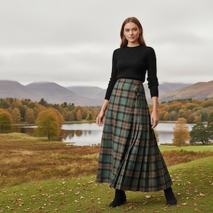 May include: A long, pleated plaid skirt in shades of green, brown, and black. The skirt is paired with a black long-sleeve sweater and black ankle boots. The background features a scenic landscape with a lake and mountains.
