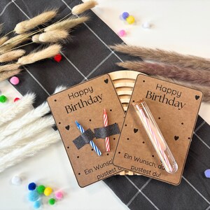 May include: Two brown cards with the text "Happy Birthday" and black polka dots. One card has two birthday candles in a clear plastic tube. The other card has two birthday candles with black tape around them. The text "Ein Wunsch, den du pustest du!" is on the bottom of the cards.