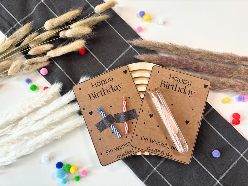 May include: Two brown cards with the text "Happy Birthday" and black polka dots. One card has two birthday candles in a clear plastic tube. The other card has two birthday candles with black tape around them. The text "Ein Wunsch, den du pustest du!" is on the bottom of the cards.