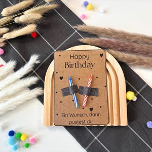 May include: A wooden rainbow arch with a brown card that says "Happy Birthday" and "Ein Wunsch, dann pustest du!" with two candles on top.