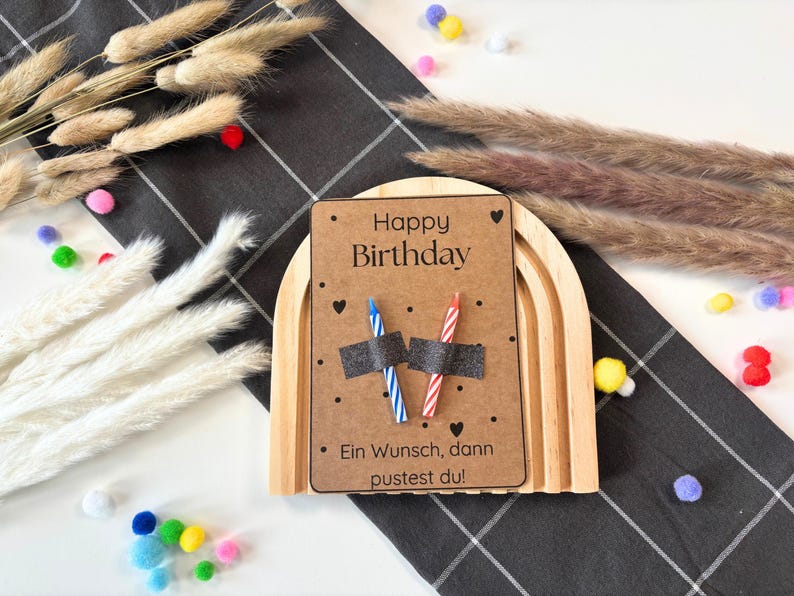 May include: A wooden rainbow arch with a brown card that says "Happy Birthday" and "Ein Wunsch, dann pustest du!" with two candles on top.