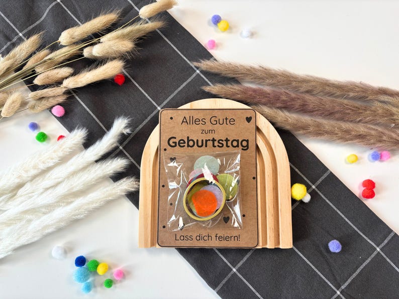 May include: A wooden rainbow arch with a card that says "Alles Gute zum Geburtstag. Lass dich feiern!" and a small bag of colourful confetti inside.