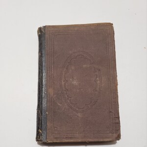 May include: A vintage brown book with a decorative design on the cover. The book has a black spine and is slightly worn.